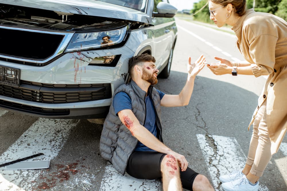 Man in pain confronts woman driver near damaged car at pedestrian crossing after road accident.